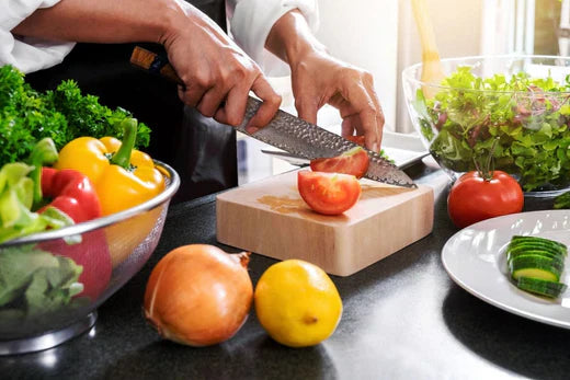 A close up of a man safely cutting a tomato with a knife 